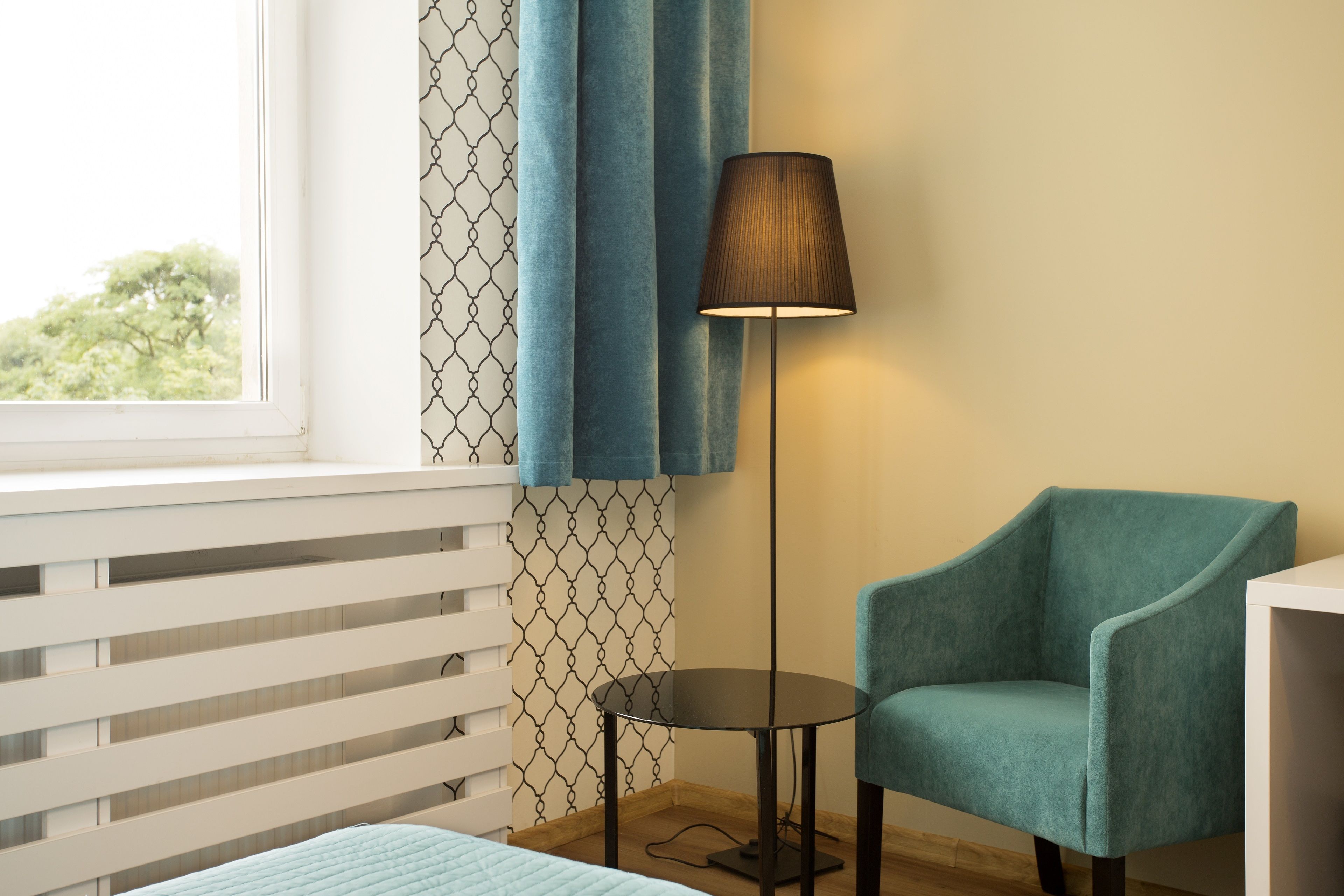 A room with a bed, a chair, a table, a lamp, and a window with curtains.