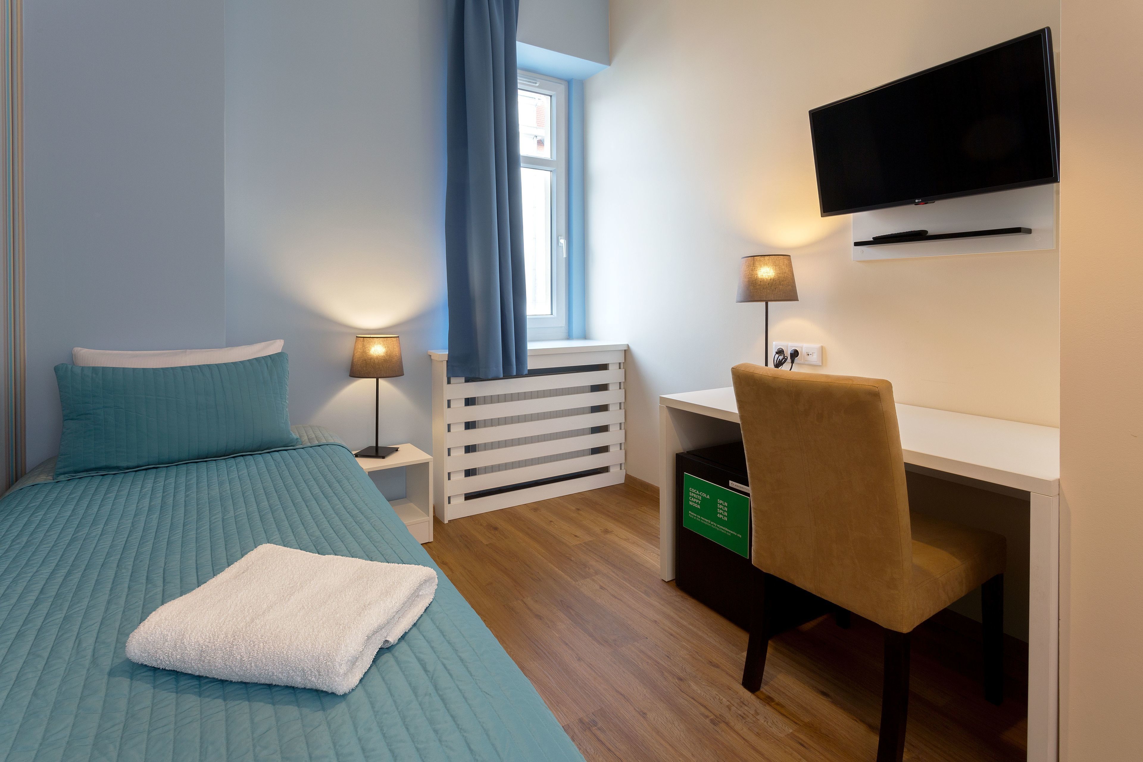 A bedroom with a bed, a desk, a chair, a TV, and a window with curtains.