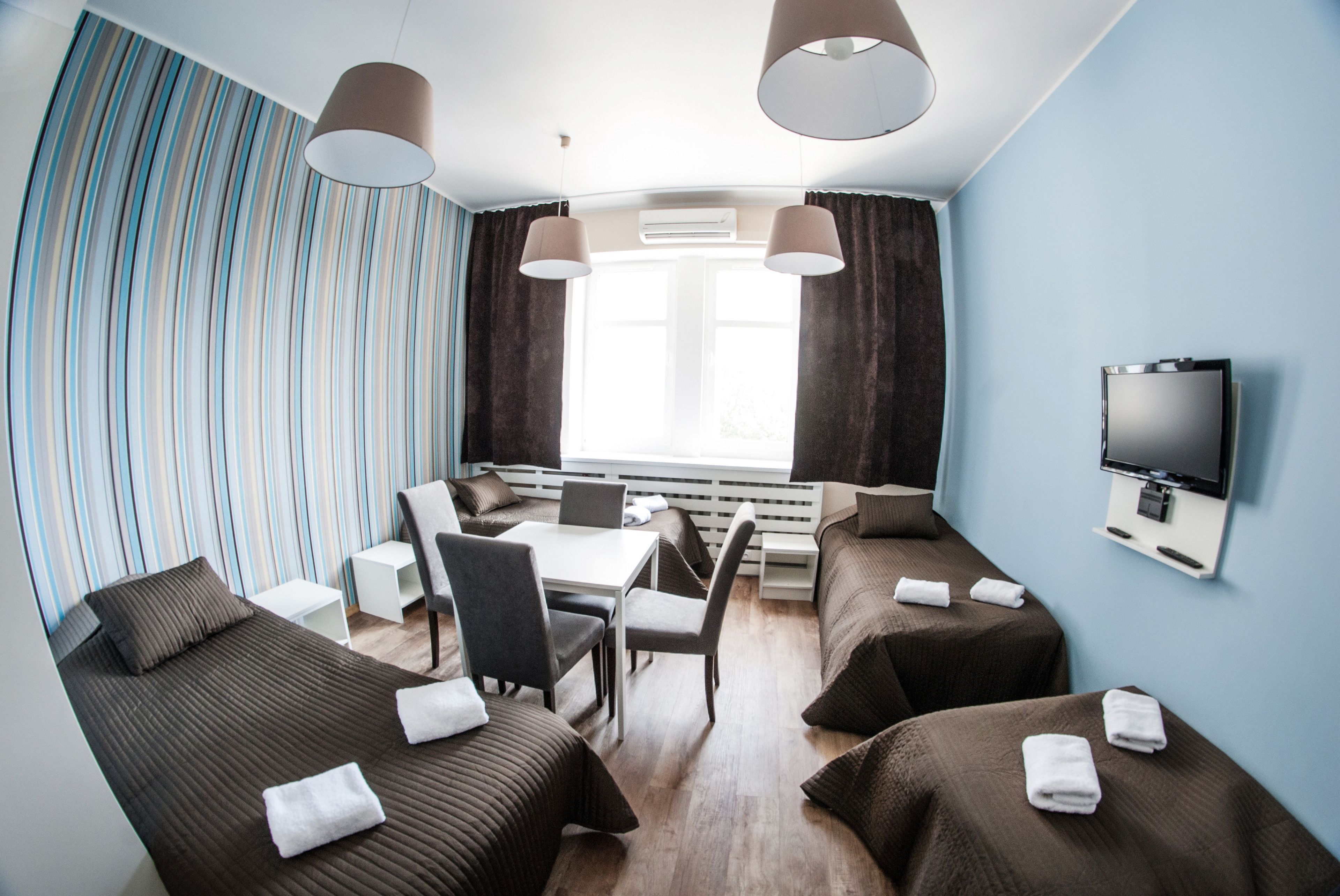 A hotel room with two beds, a desk, chairs, a TV, and a window with curtains.