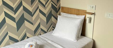 Una cama individual con sábanas blancas, cabecera de madera y pared con estampado en zigzag.