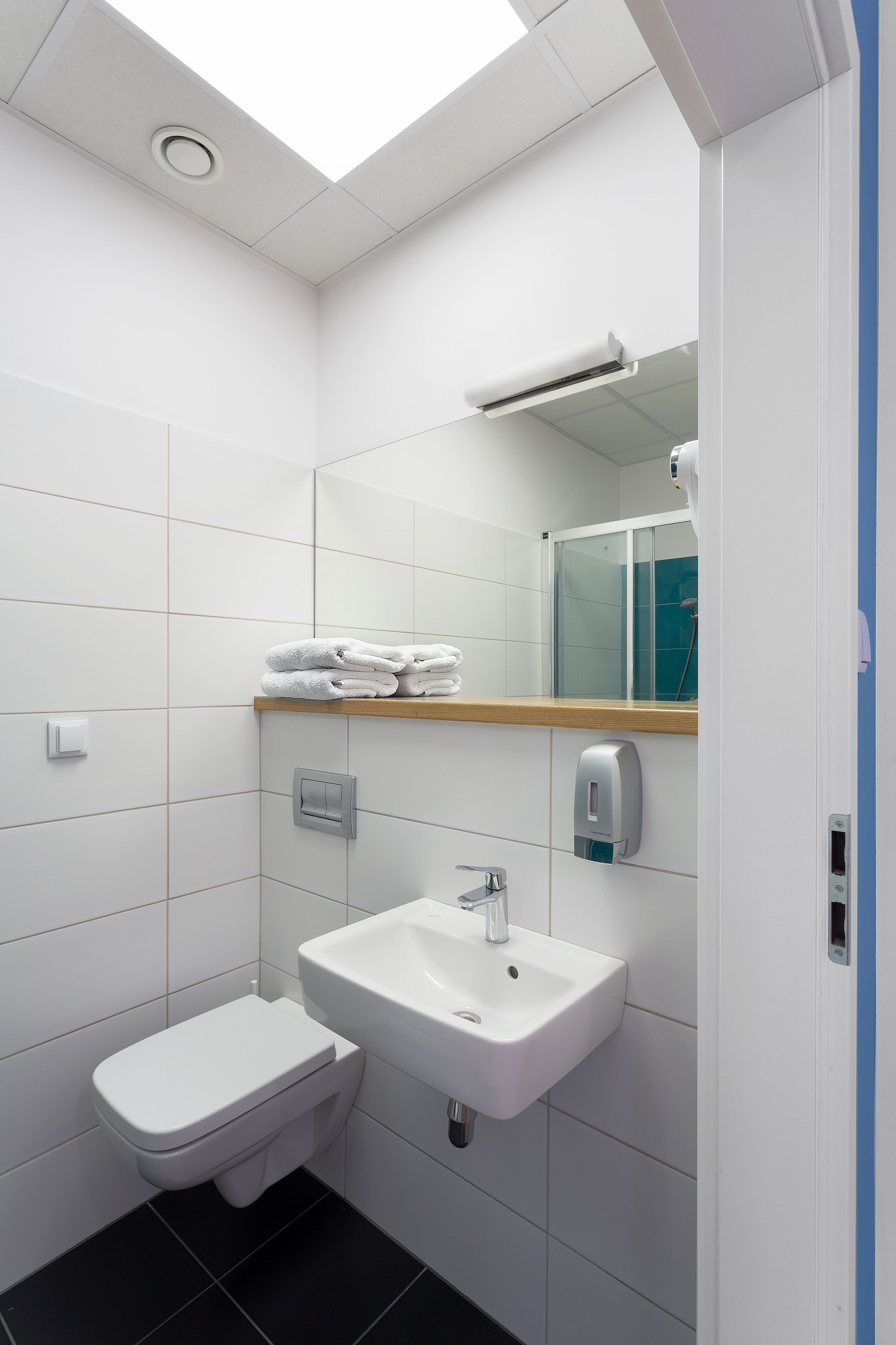 A modern bathroom with white tiles, a white sink, a toilet, a mirror, and a towel rack.