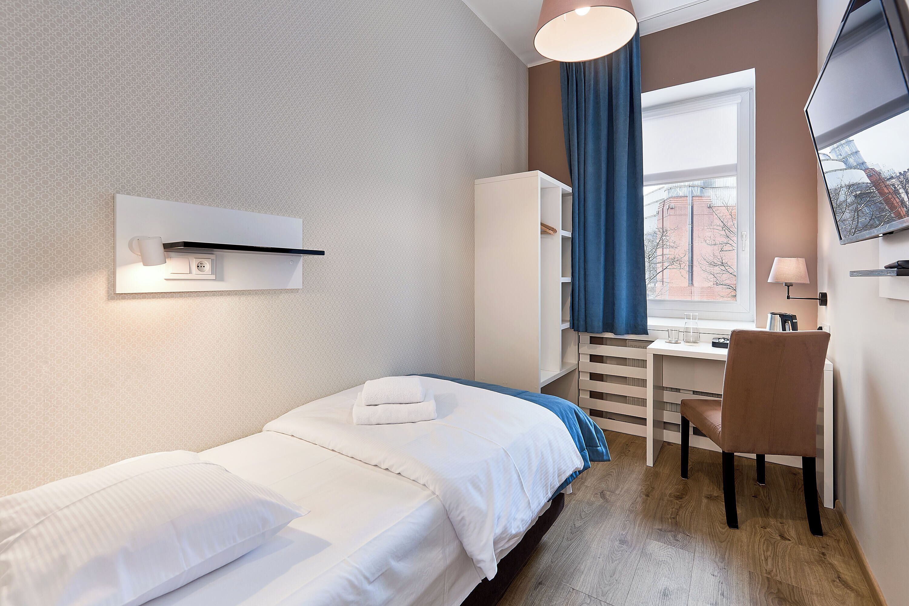 A hotel room with a bed, a desk, a chair, a TV, and a window with curtains.