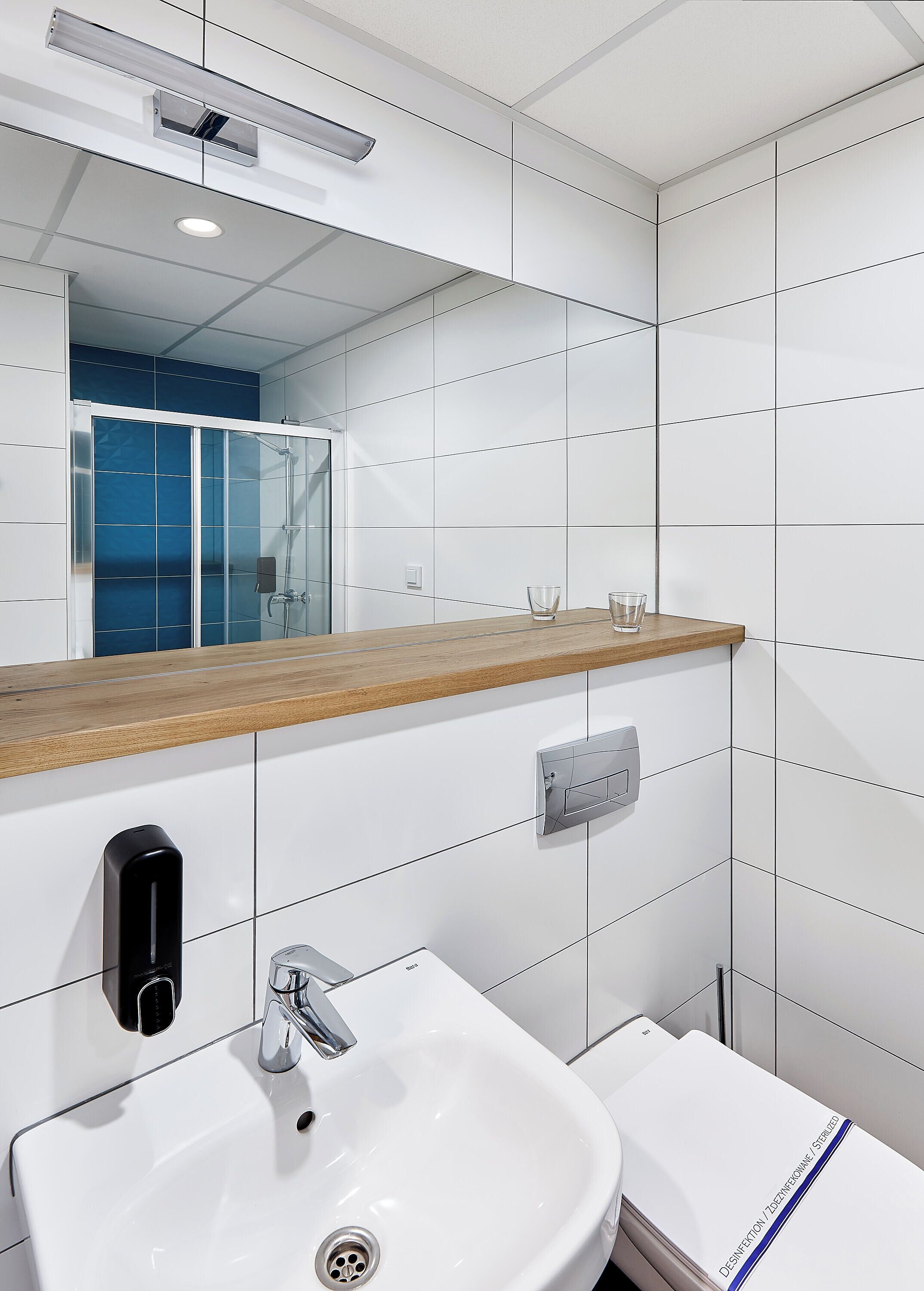 A modern bathroom with a white sink, mirror, and wooden countertop.