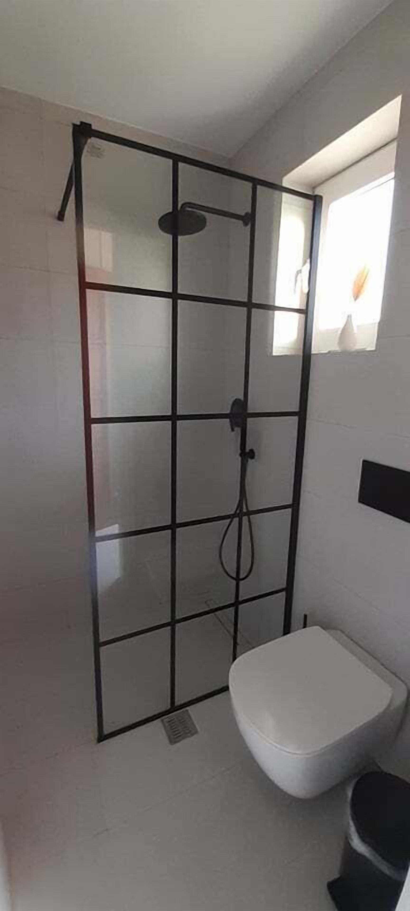 Ein Badezimmer mit einer Duschkabine, einer weißen Toilette und einem kleinen Fenster.