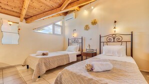 Quarto com duas camas, vigas de madeira no teto, uma janela e luminárias fixadas na parede.