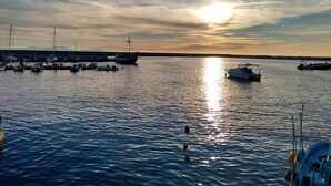 Uma marina com barcos atracados no cais, águas calmas e um pôr do sol ao fundo.