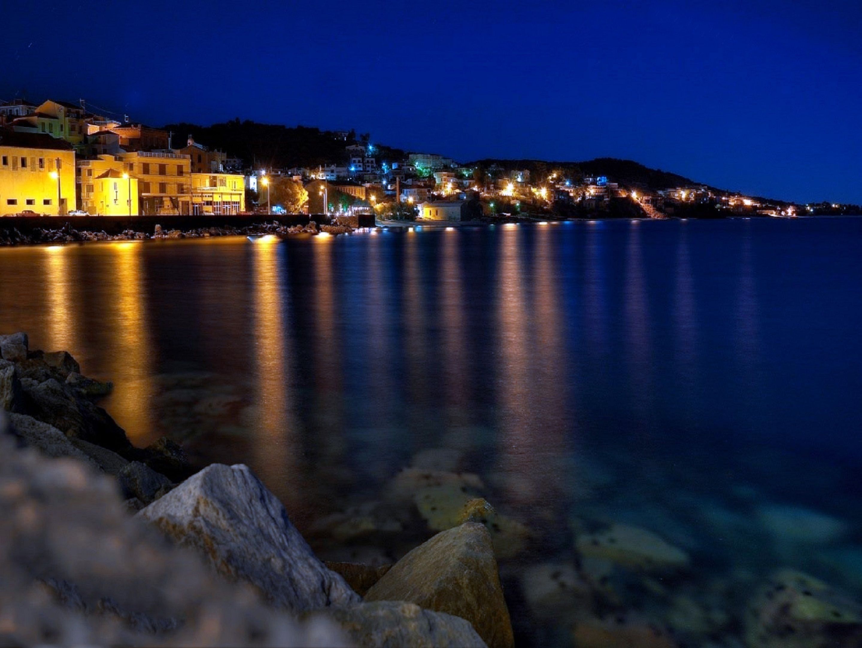 Un pueblo costero de noche, con edificios iluminados a lo largo del paseo marítimo.