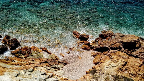 Uma costa rochosa com água cristalina e uma faixa de areia de pedrinhas.