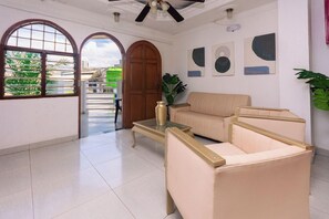 Un salón amplio con un sofá color beige, una mesa de centro de vidrio y un ventilador de techo.