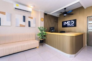 A hotel reception area with a reception desk, a sofa, a clock, and a plant.