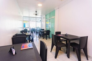 En hotellrestaurang med flera bord och stolar, en takfläkt och stora fönster som släpper in naturligt ljus.