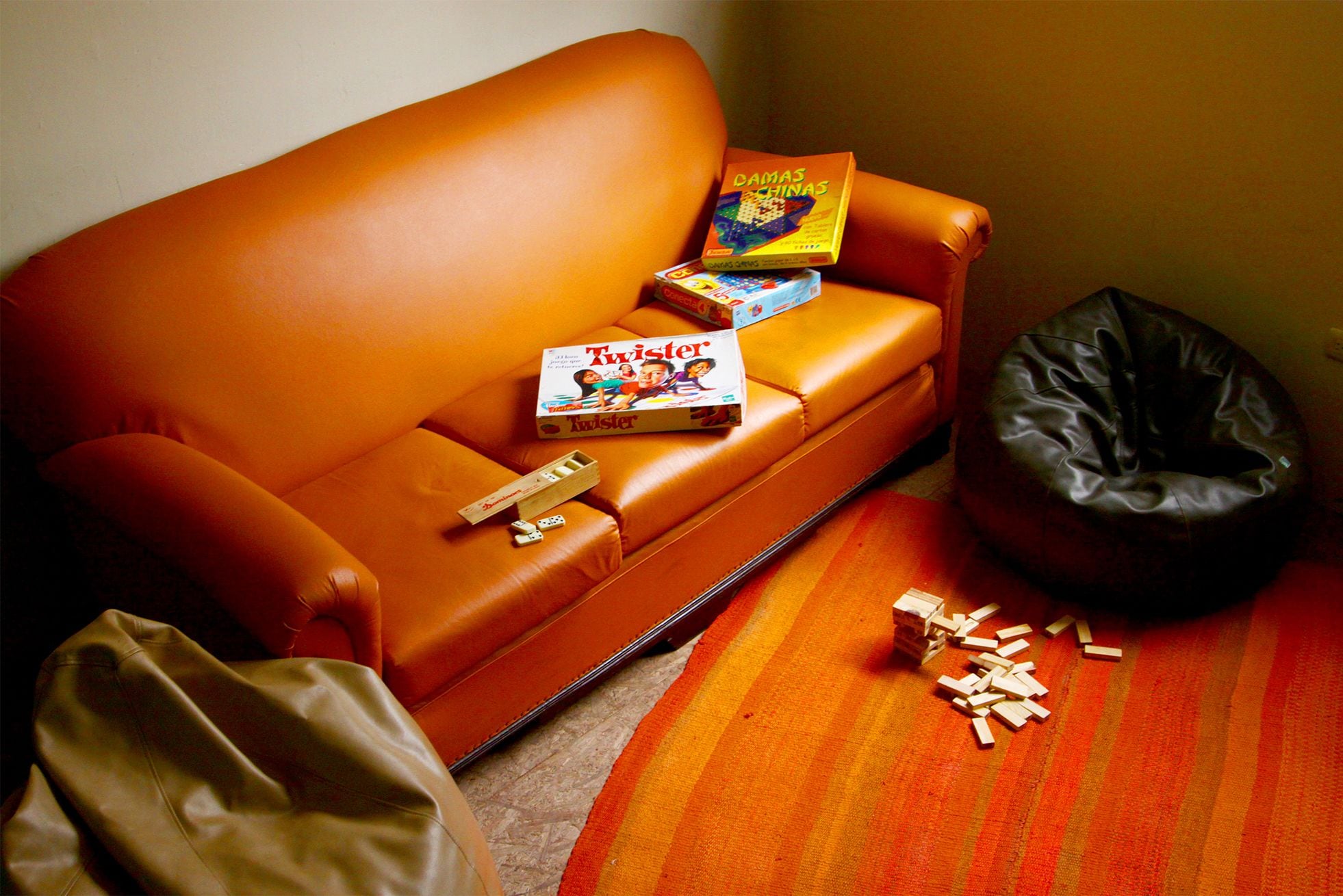 A small, orange sofa with a box of Twister and a black bean bag chair.