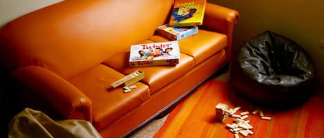 Un sofá pequeño naranja con un juego de Twister y un sillón inflable negro.