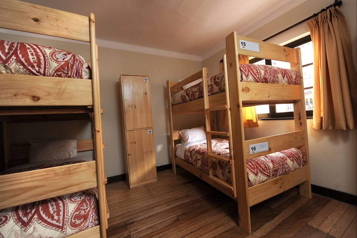 A dormitory room with bunk beds, wooden lockers, and a window with curtains.