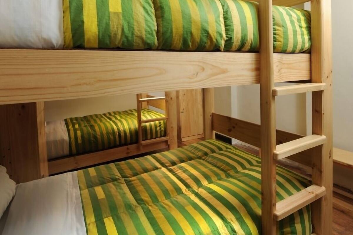 A bunk bed with green and white striped bedding, wooden headboard, and a ladder.