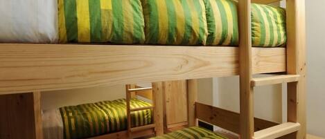 A bunk bed with green and white striped bedding, wooden headboard, and a ladder.