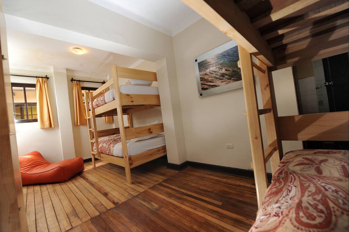 A bunk bed room with wooden flooring, a red bean bag chair, and a framed picture on the wall.