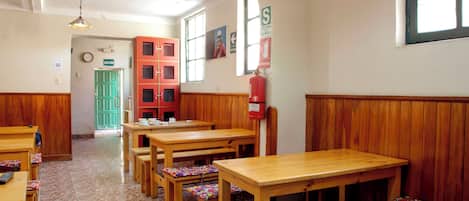 A room with wooden benches and tables, a green door, and a fire extinguisher on the wall.