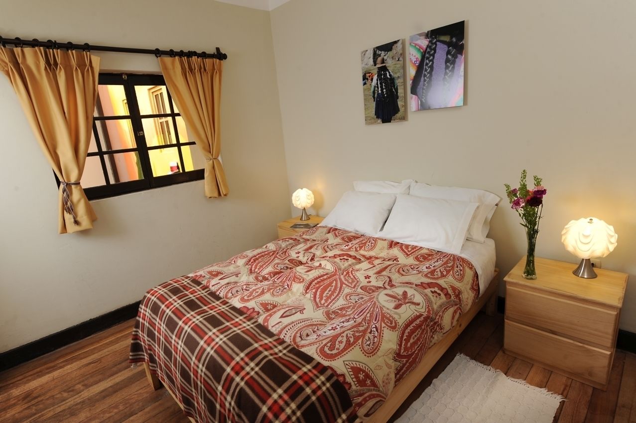 Un dormitorio con una cama, dos mesitas de noche, una lámpara de noche, una ventana con cortinas y decoración en la pared.