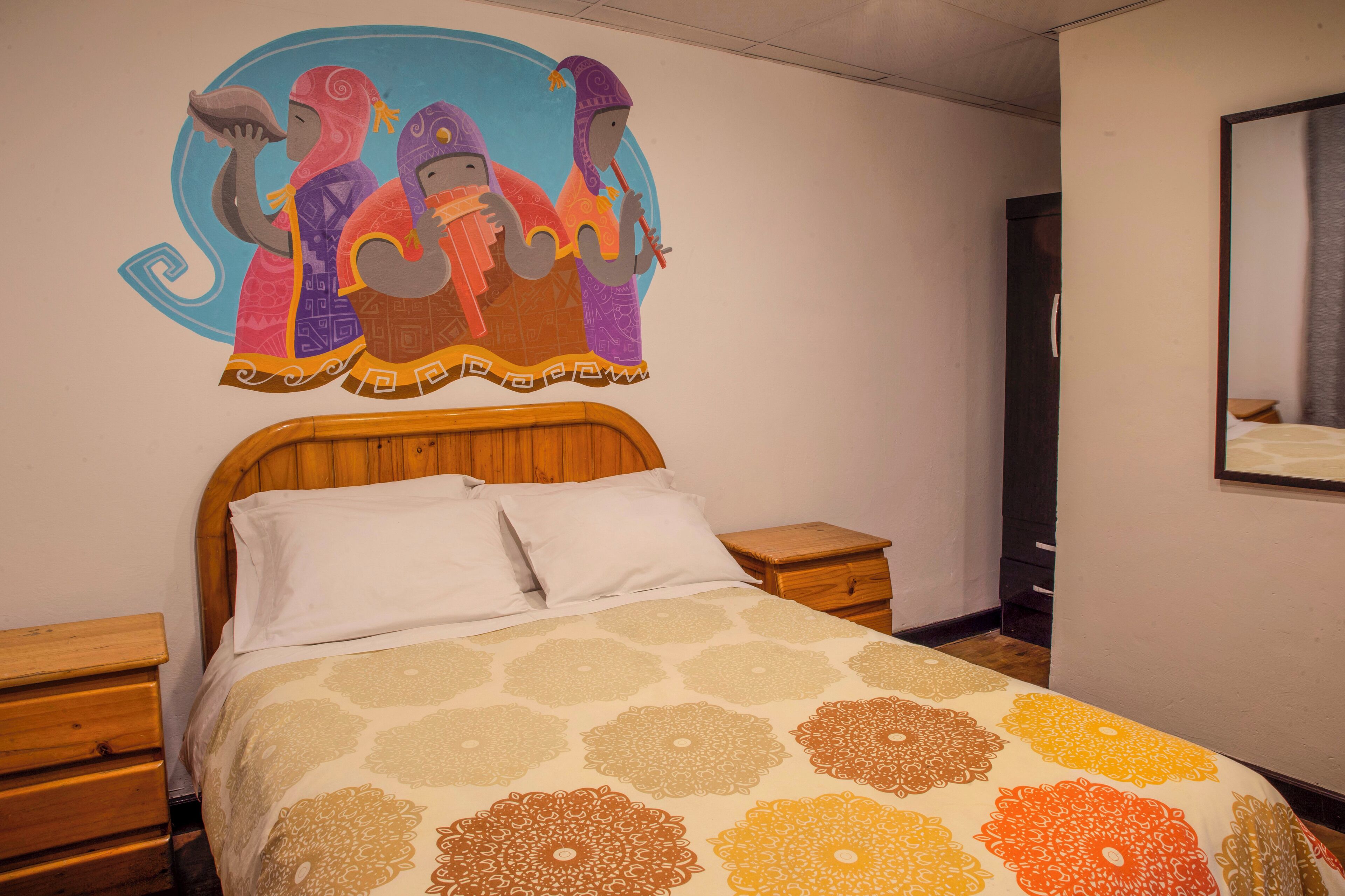 A bedroom with a bed, wooden nightstands, a wall mural, and a mirror.