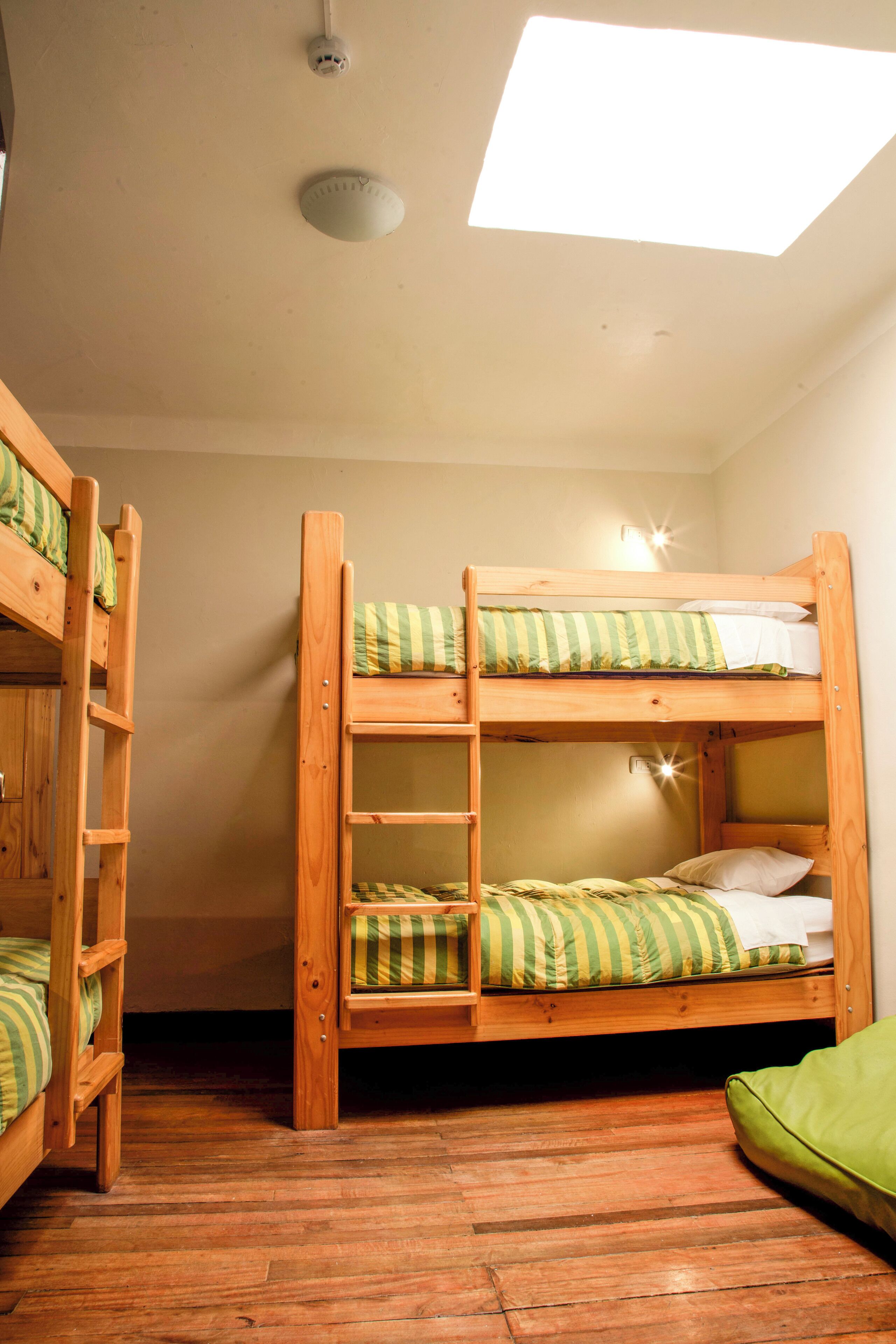 Une chambre avec un lit superposé, une lucarne, un plancher en bois et un coussin vert.