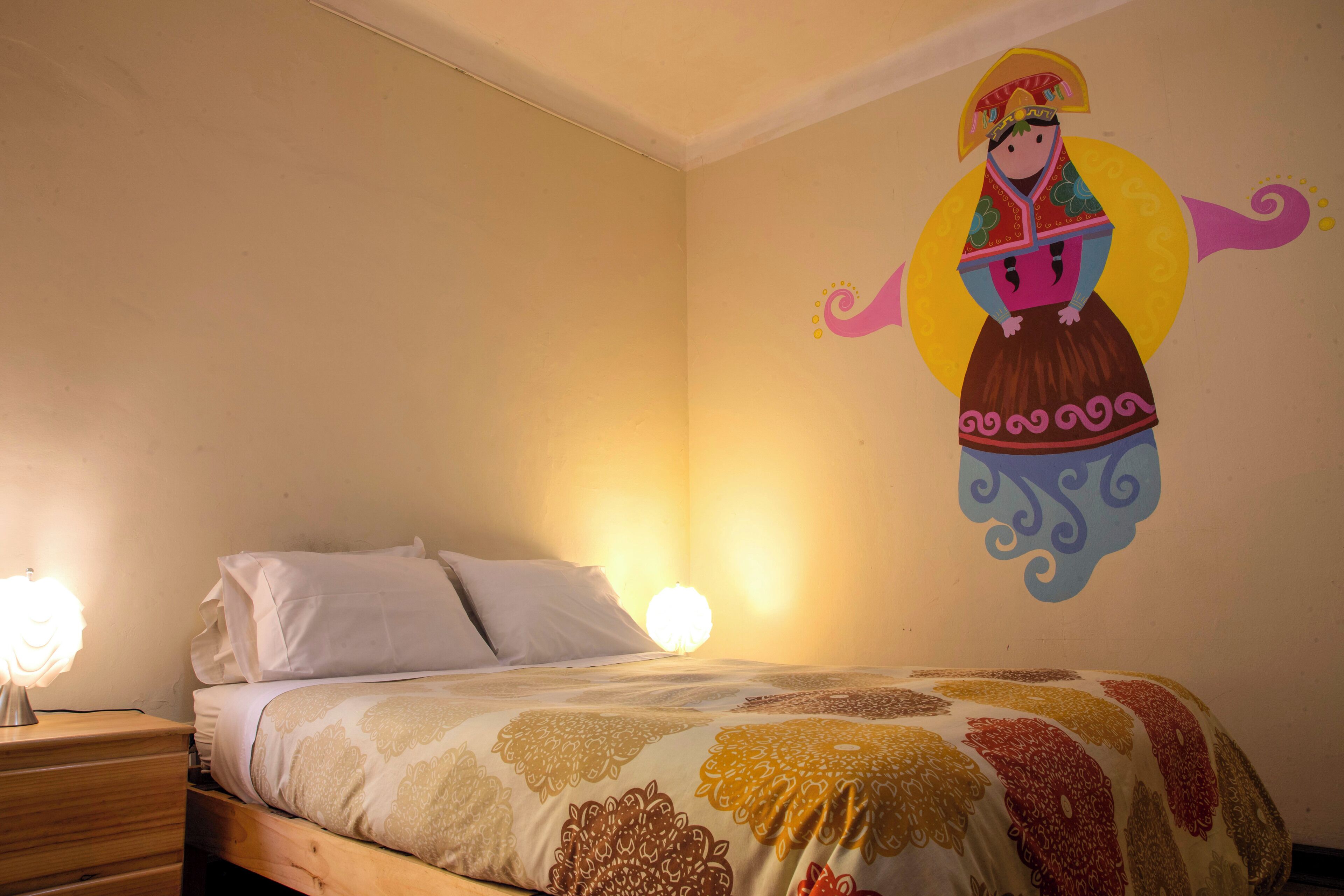 Un dormitorio con cama, mesita de noche, un mural en la pared y una lámpara de pared.