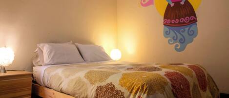 Un dormitorio con cama, mesita de noche, un mural en la pared y una lámpara de pared.