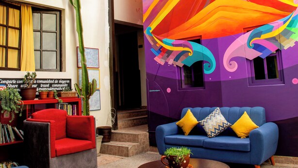 Un salón vibrante con un mural colorido, un cactus y un sofá azul con cojines amarillos.
