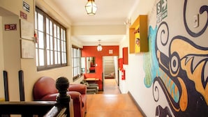 Un pasillo con suelo de madera, una zona de estar con asientos rojos y un mural en la pared.