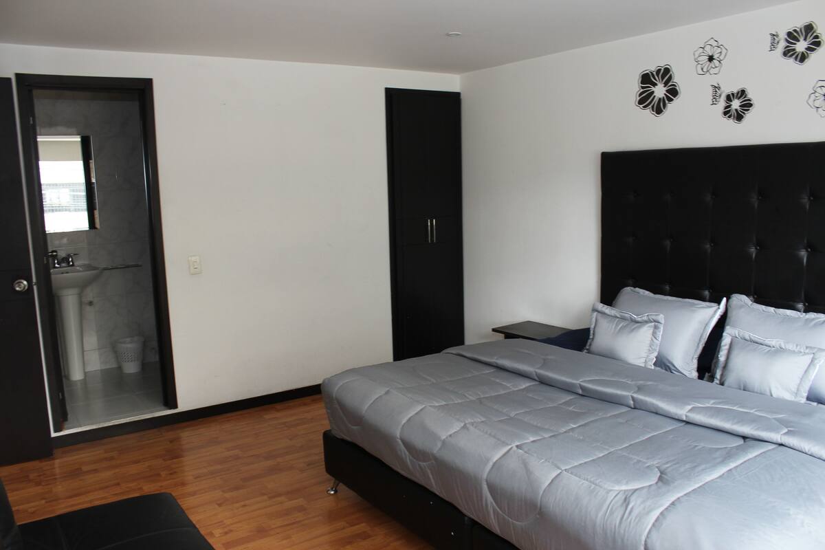Ein Schlafzimmer mit Bett, Kleiderschrank, Nachttisch und angrenzendem Badezimmer.