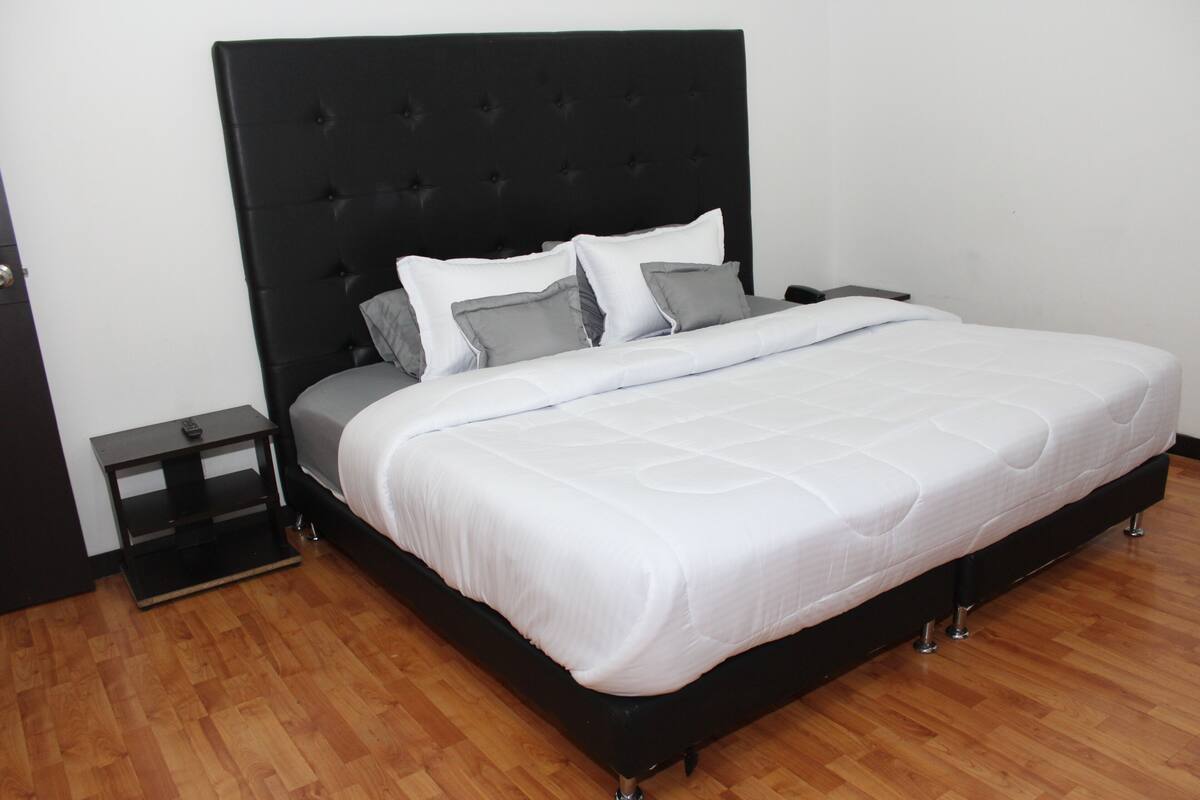 Ein Bett mit schwarzem Kopfteil, weißer Bettwäsche und Holzboden.