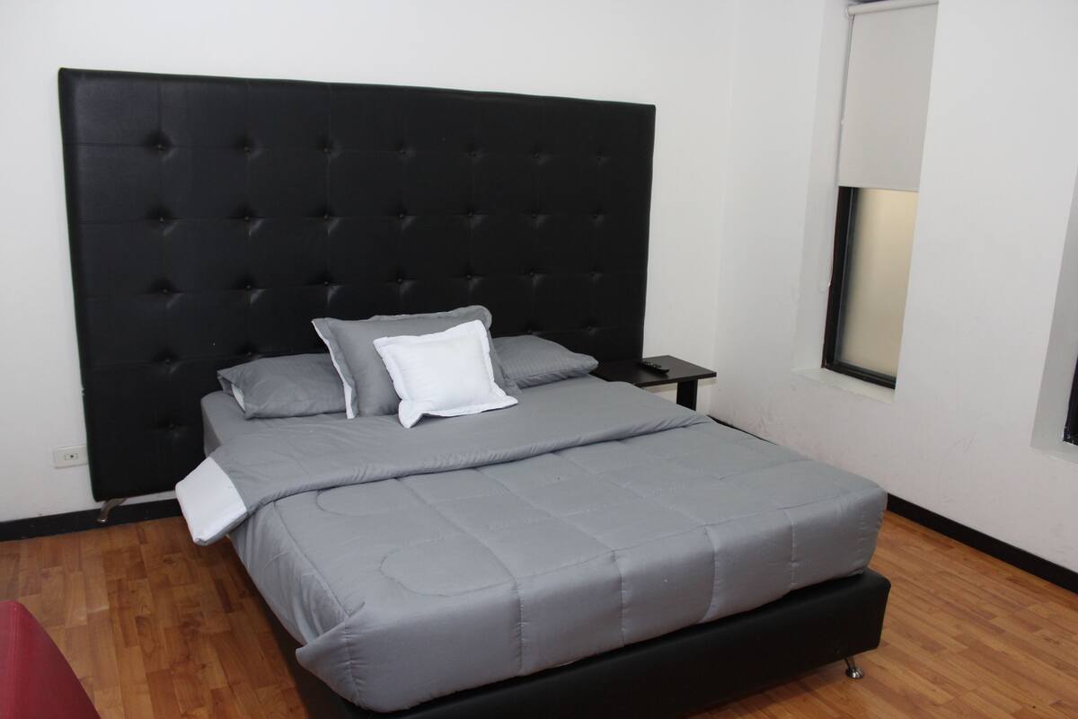 Ein Bett mit einer gepolsterten Kopfteile, grauer Bettwäsche und einem kleinen Nachttisch.