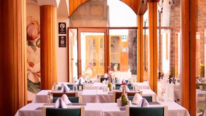 A restaurant with wooden interior, tables set with white tablecloths, and green upholstered chairs. - Hotel Monasterio San Pedro (Cusco)