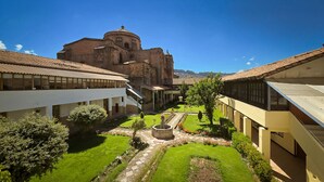 A courtyard with a central fountain, surrounded by buildings with tiled roofs and a large church in the background. - Hotel Monasterio San Pedro (Cusco)