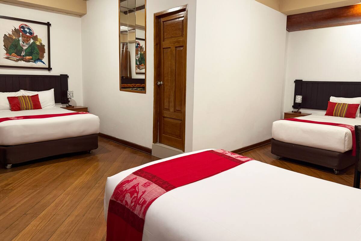 Ein Hotelzimmer mit zwei Betten, Holzboden, einer Holztür und einem Spiegel.