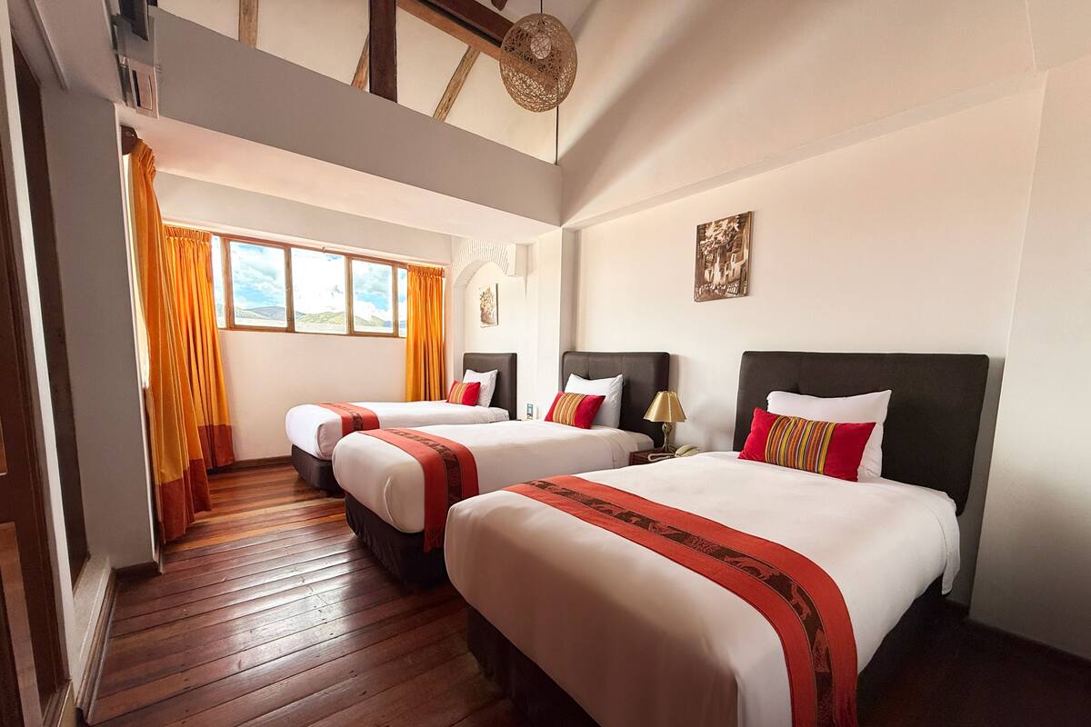 Ein Hotelzimmer mit zwei Betten, Holzboden, einer Treppe und einem großen Fenster mit Vorhängen.