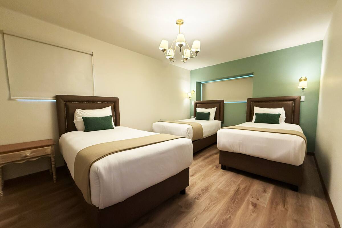 Ein Hotelzimmer mit drei Betten, Holzboden, einem großen Spiegel und einer Kronleuchter.