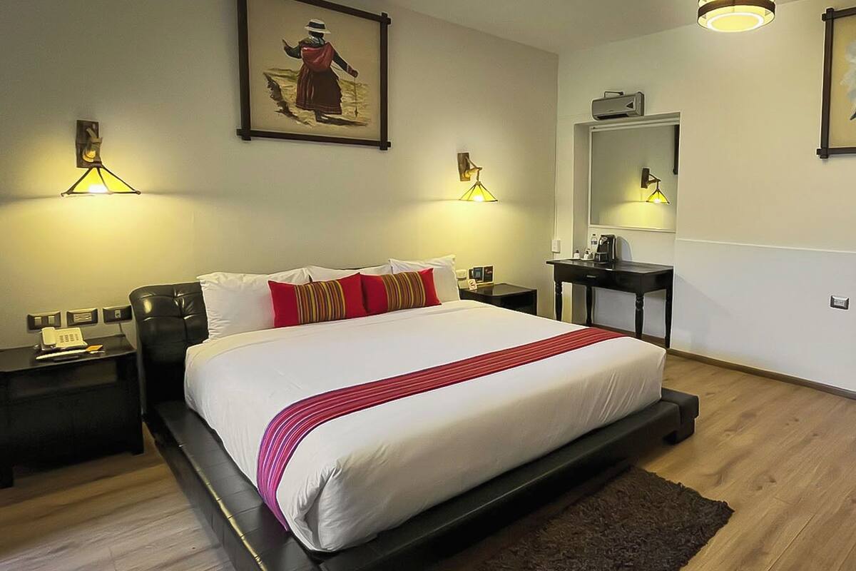 Ein Hotelzimmer mit einem großen Bett, Nachttischen, einem Schreibtisch, einem Spiegel und einem Bild an der Wand.