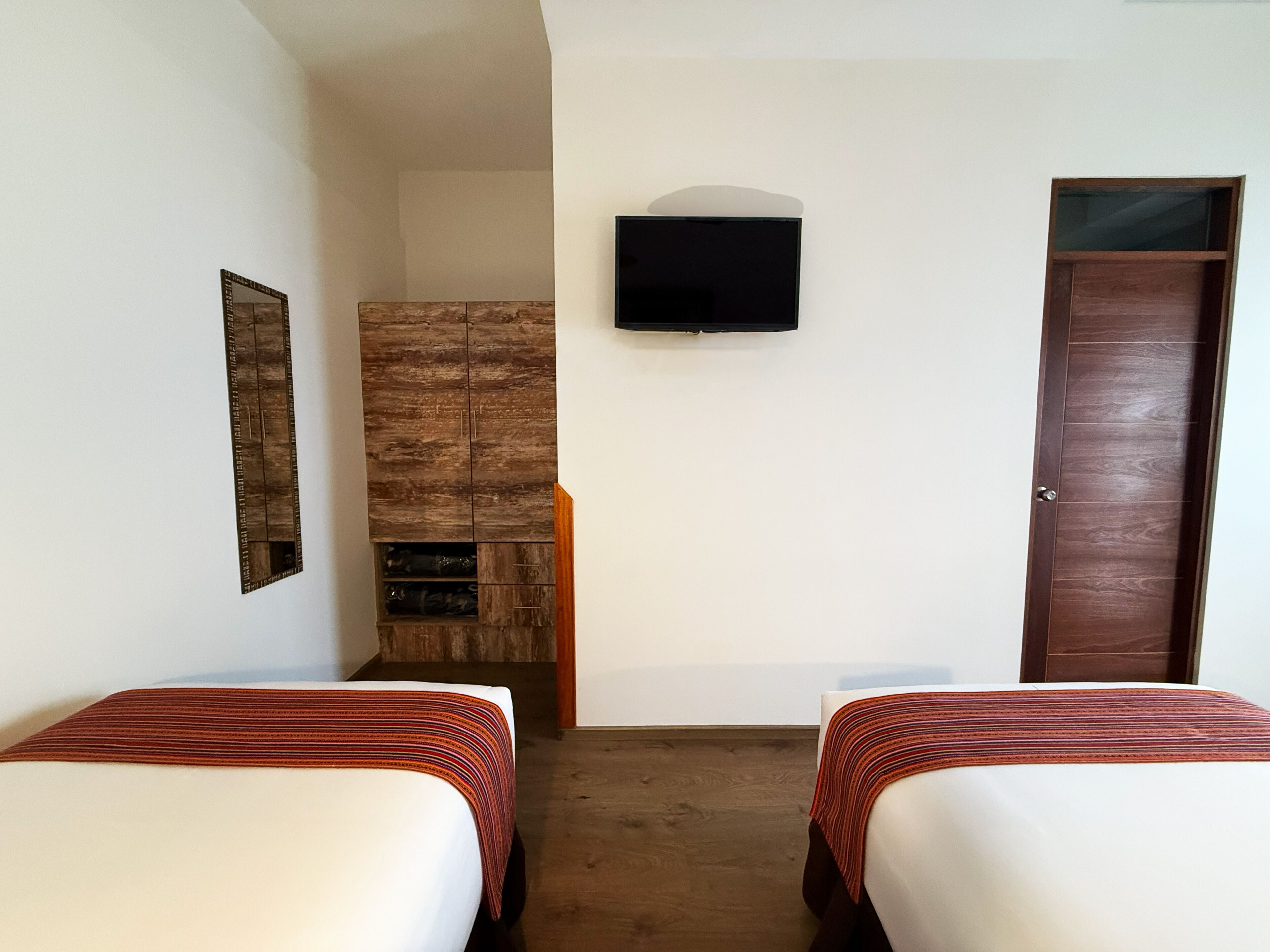 A room with two beds, a TV on the wall, a wooden cabinet, and a door.