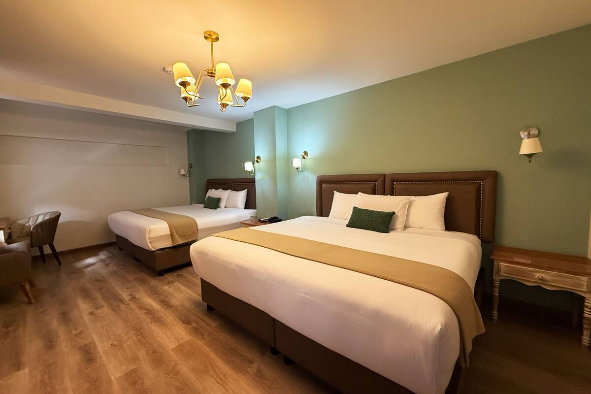 Ein Hotelzimmer mit zwei Betten, einem Sessel, Holzboden und einer Chandelier.