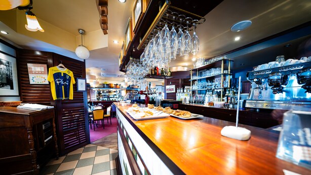 A bar area with a counter, glasses hanging above, and a sports jersey on the wall. - Au Relais Nivernais (Nevers)