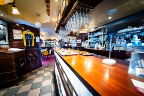 A bar area with a counter, glasses hanging above, and a sports jersey on the wall. - Au Relais Nivernais (Nevers)