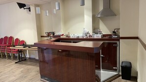 A modern kitchen with a wooden counter, a sink, and a stove. There are red chairs and a table in the background. - Au Relais Nivernais (Nevers)