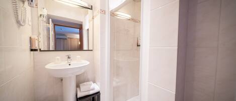A modern bathroom with a pedestal sink, a glass shower enclosure, and a mirror with a towel rack.