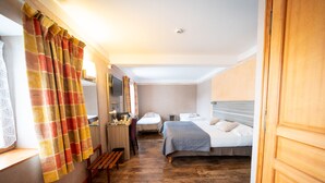 A hotel room with a wooden floor, a bed with a gray blanket, a desk with a chair, and a television on the wall. - Au Relais Nivernais (Nevers)