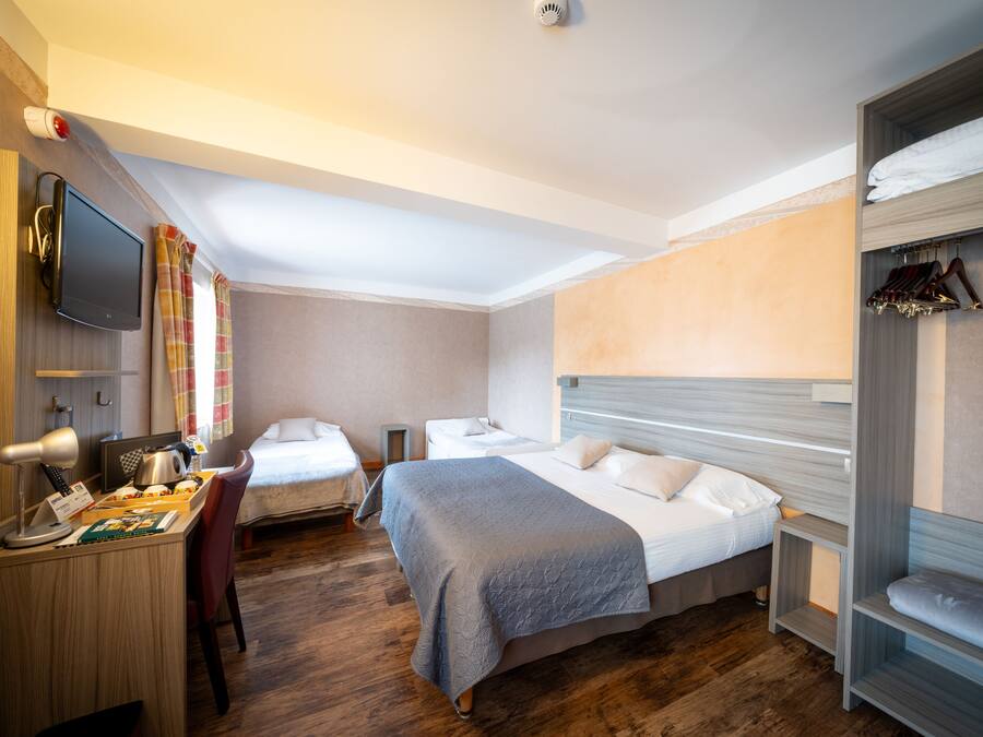 Une chambre d’hôtel avec deux lits, un bureau avec un ordinateur, un téléviseur fixé au mur et une armoire avec des vêtements suspendus.