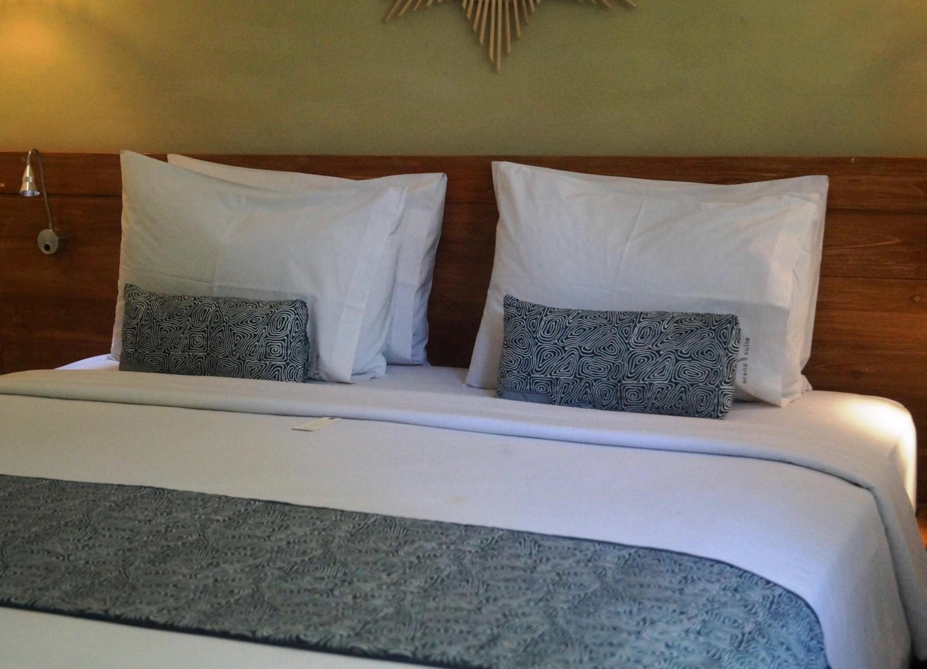 A bed with white pillows and patterned throw pillows, a wooden headboard, and a textured blanket.