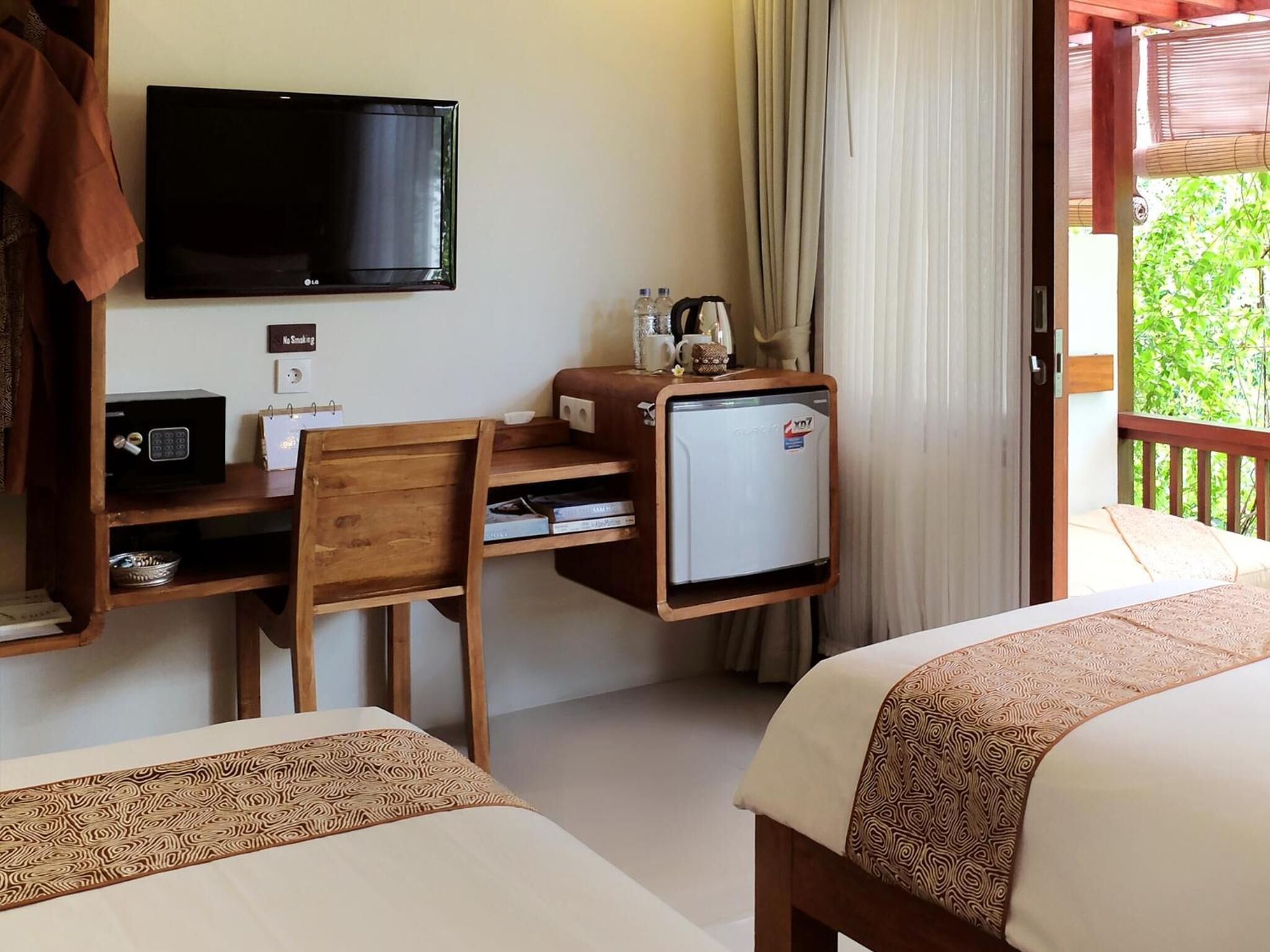 A hotel room with a desk, a television, a mini-fridge, a chair, and two beds.
