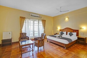 A hotel room with a bed, two chairs, a table, a ceiling fan, and a window with curtains.