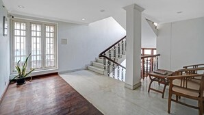 A spacious room with a wooden floor, a staircase with a wrought iron railing, and a seating area with wooden furniture. - Fort Manor (Kochi)